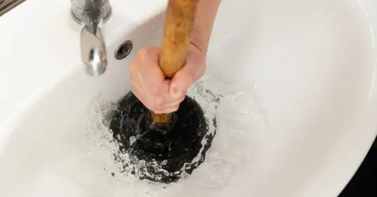 Man uses the plunger to unclog the sink drain